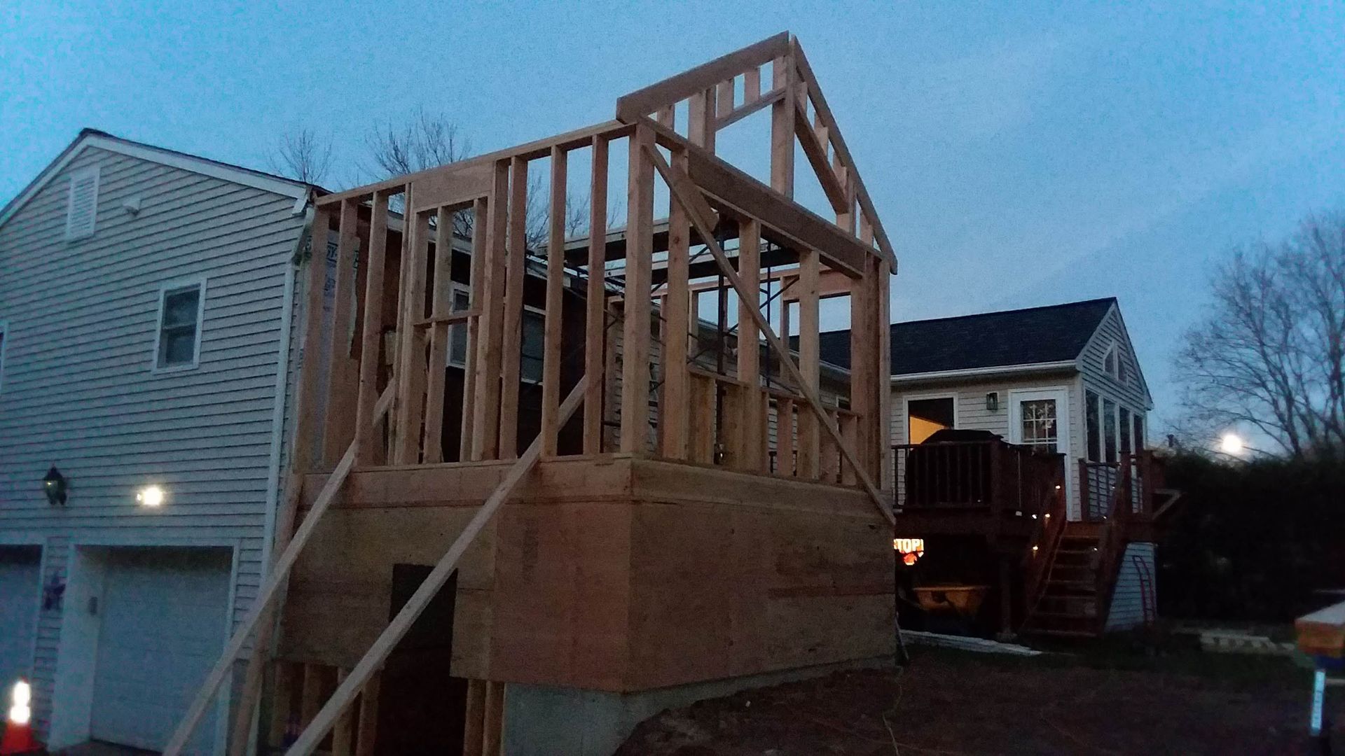 Construction of a wooden house addition next to an existing home, visible during twilight.
