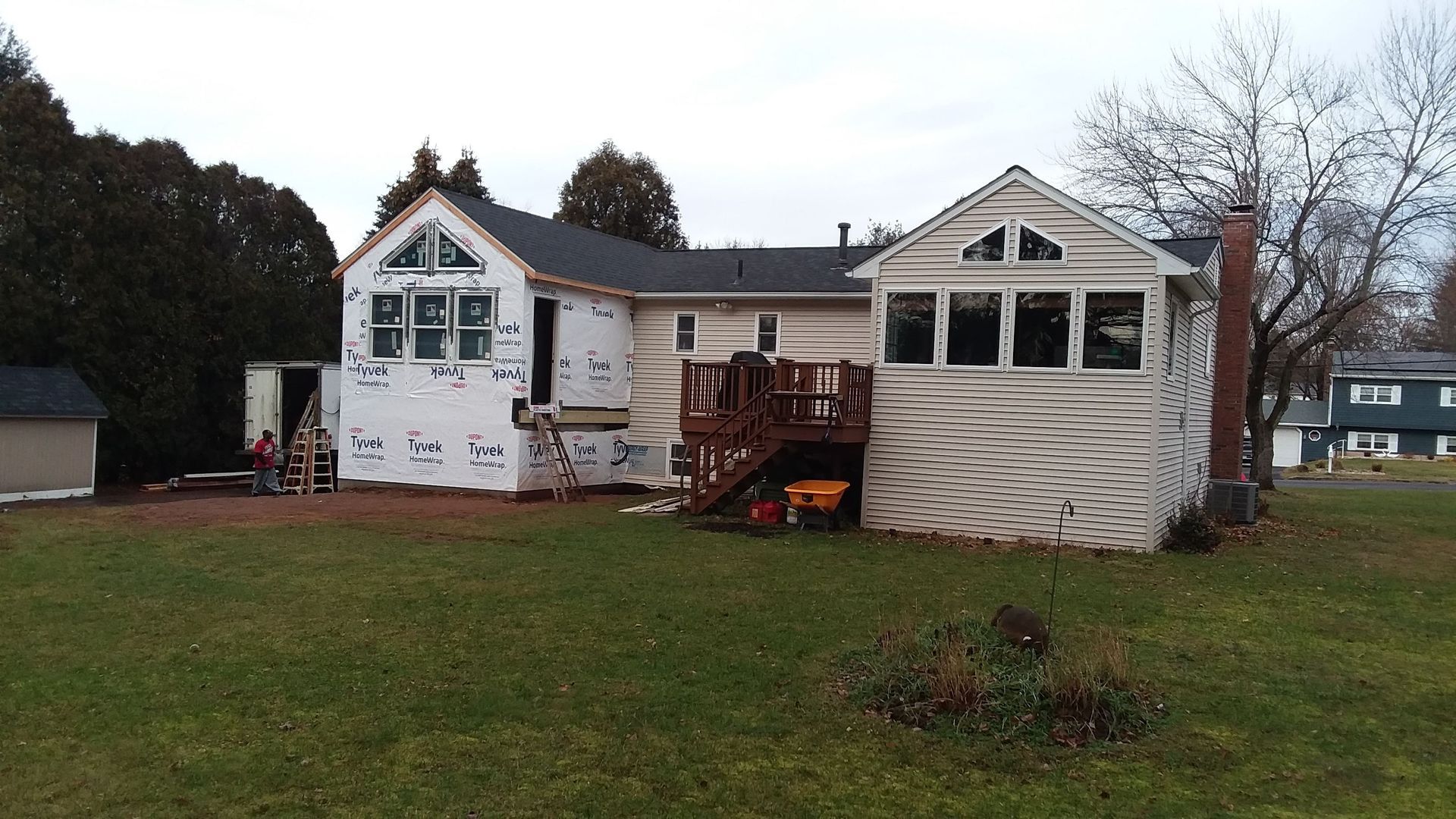 Backyard view of a house undergoing renovations; white siding and exposed framework, with a deck.