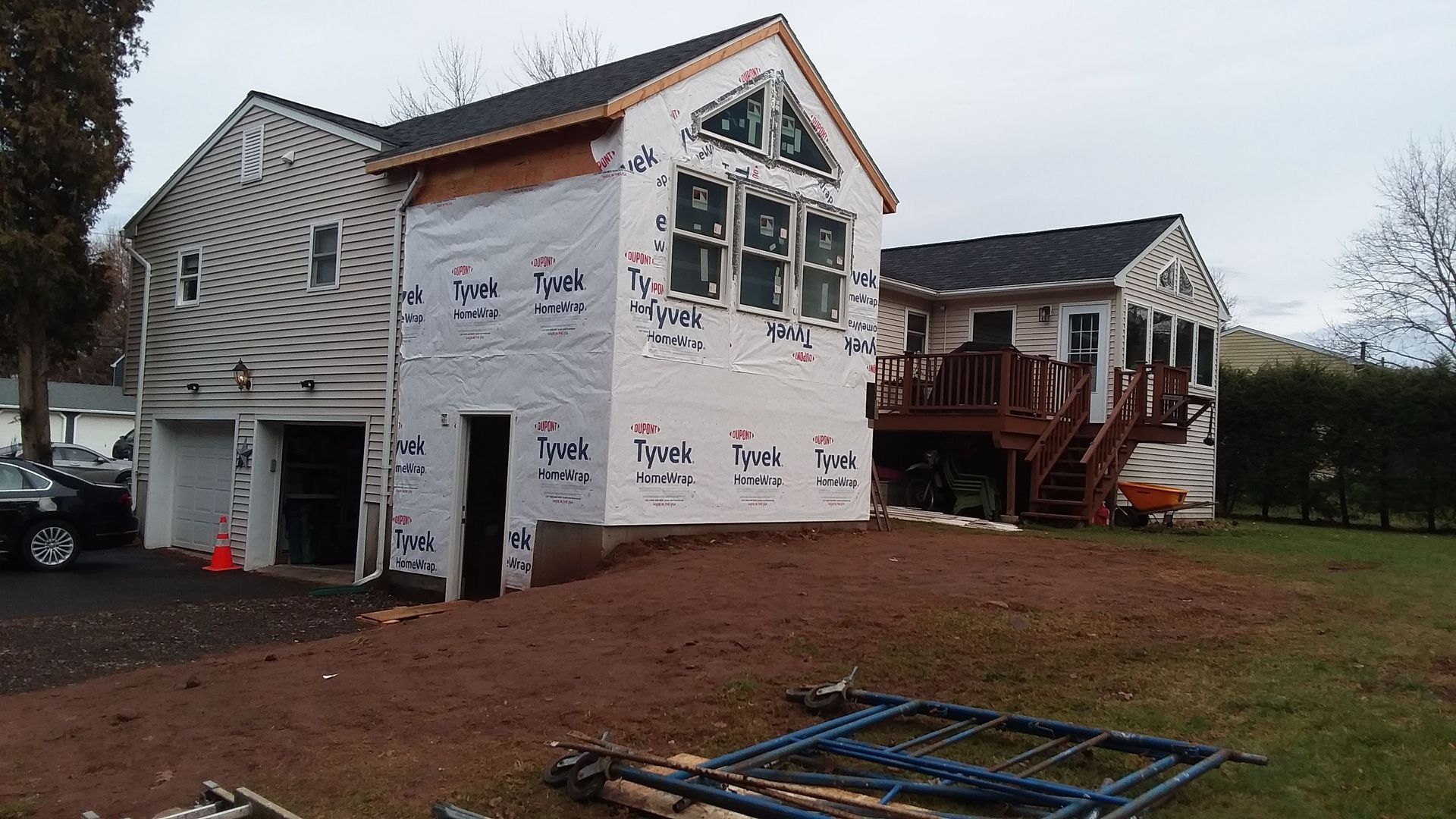 House under construction with attached garage and deck. Exterior wrapped in white with dark roof.