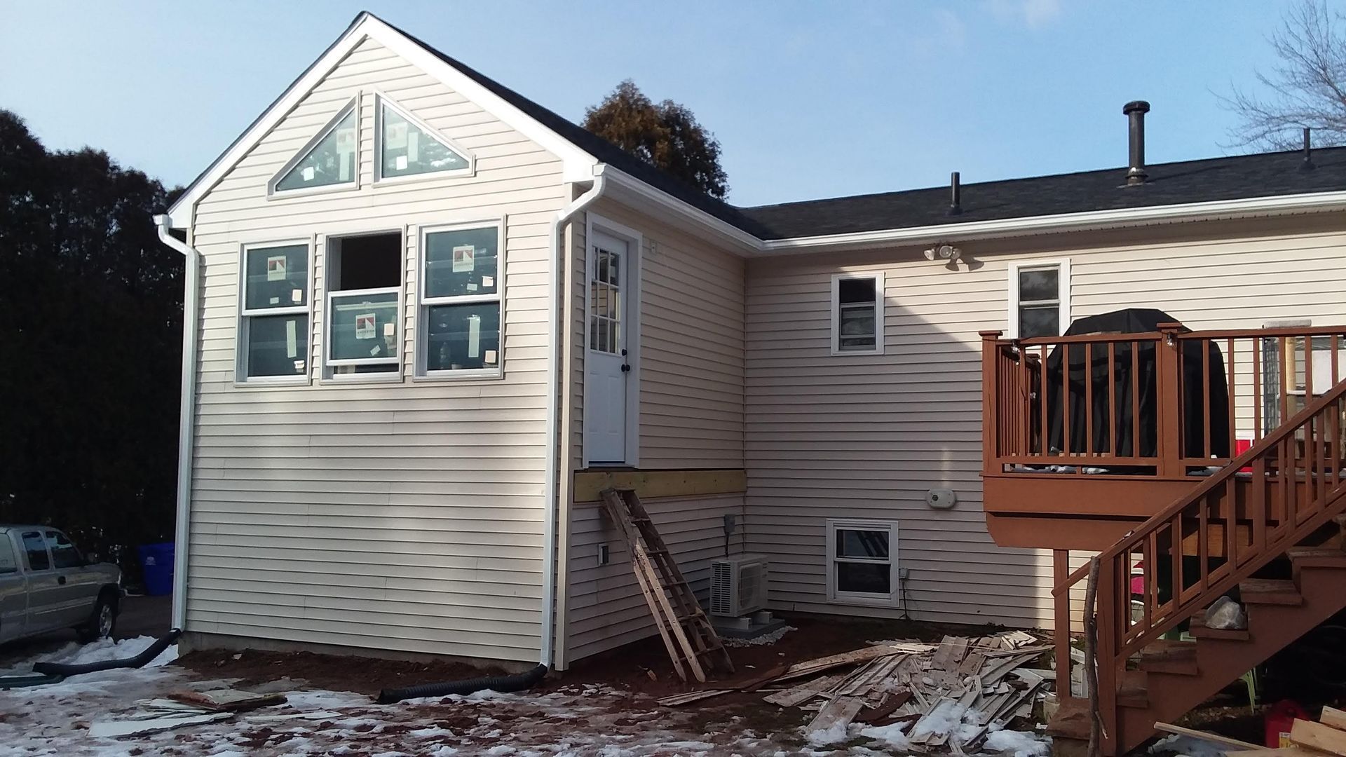 House addition with new siding, windows, and deck, surrounded by snow.
