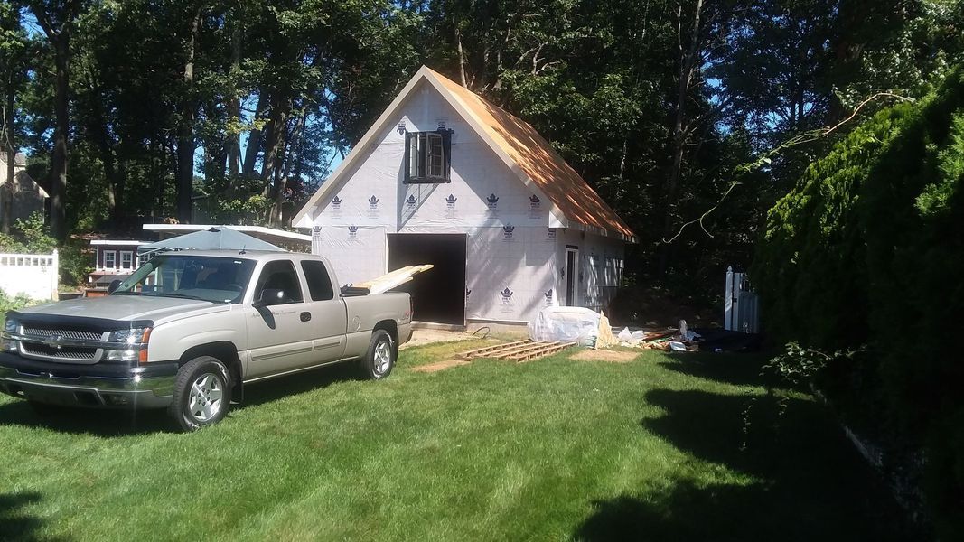 A silver pickup truck parked next to a barn-style structure under construction in a grassy yard.