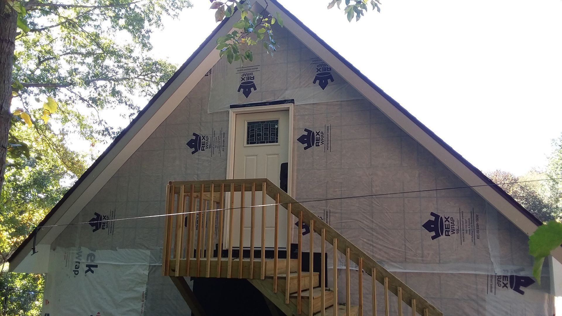 A-frame building exterior with wood stairs leading to a white door. The building is covered in silver wrap.