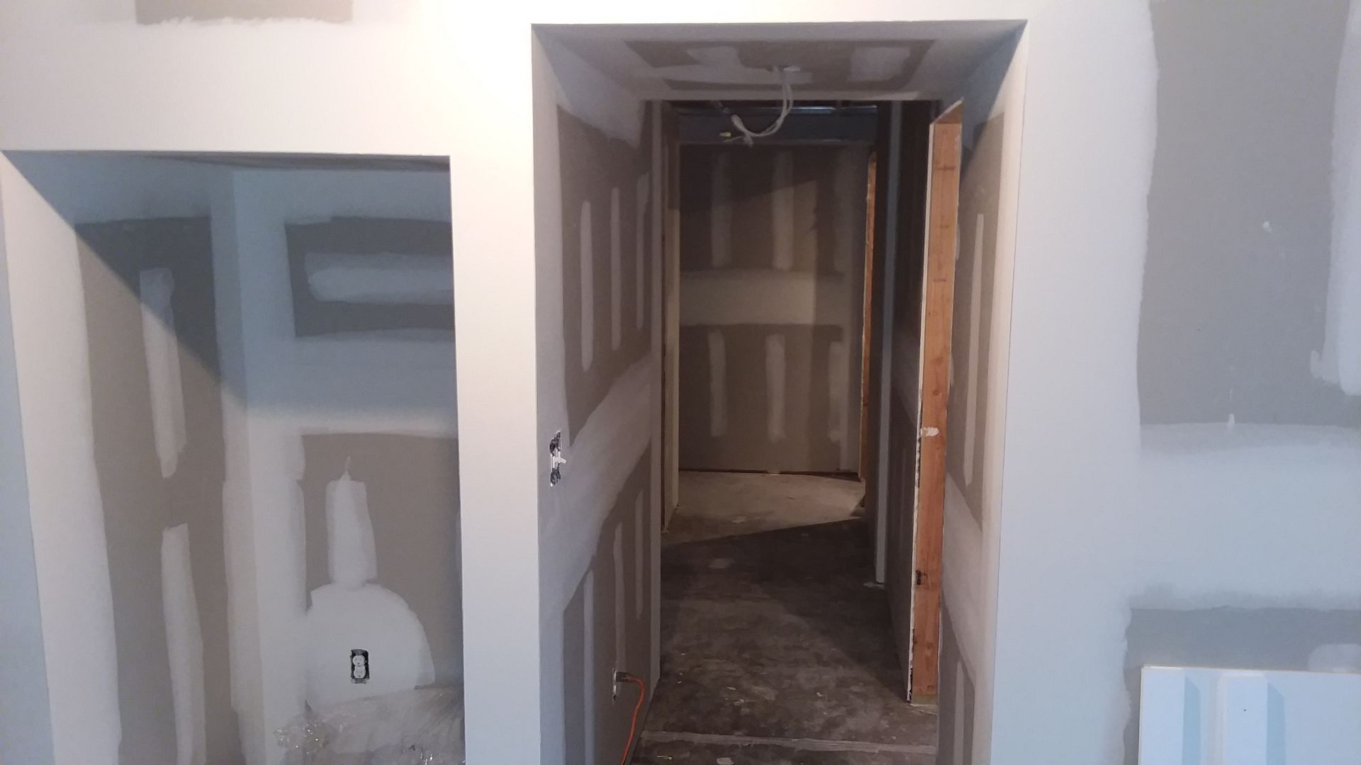 Interior view of a hallway under construction, with drywall, a door frame, and unfinished closet.