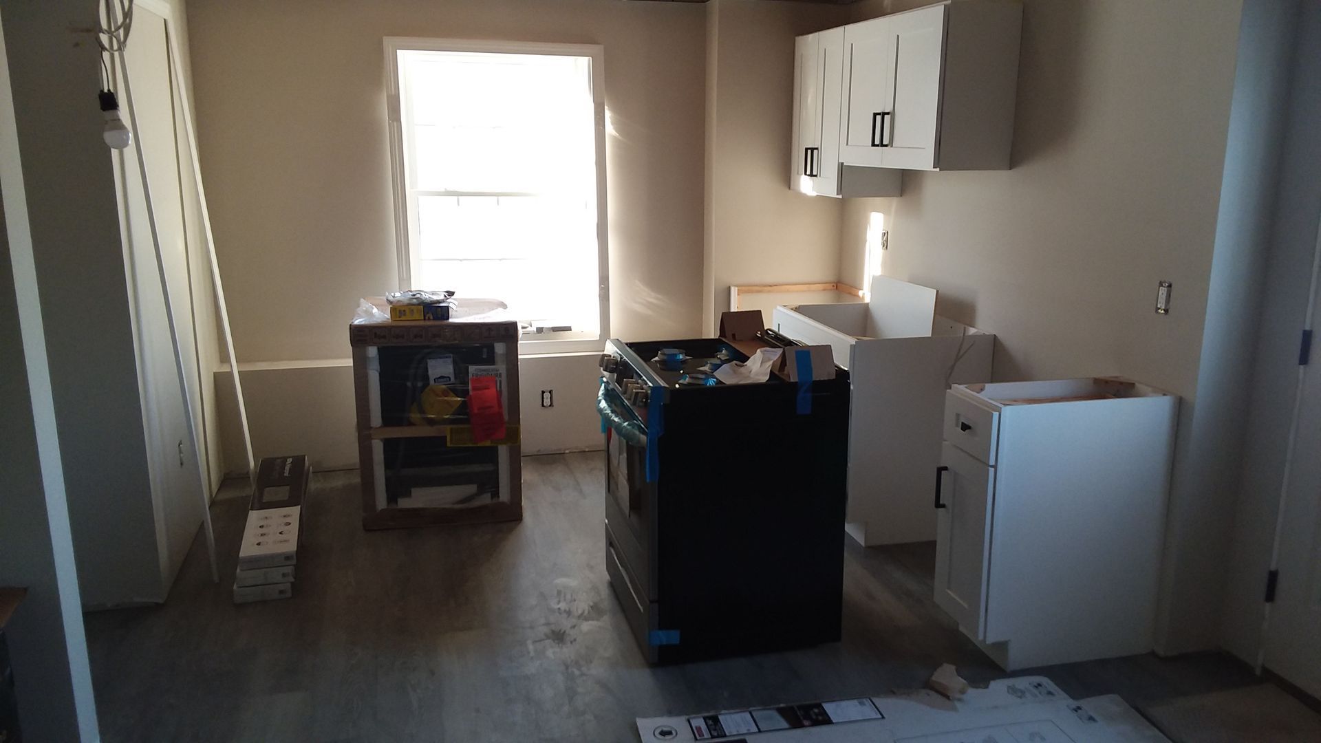 Kitchen undergoing renovation with cabinetry, appliances, and construction materials visible.