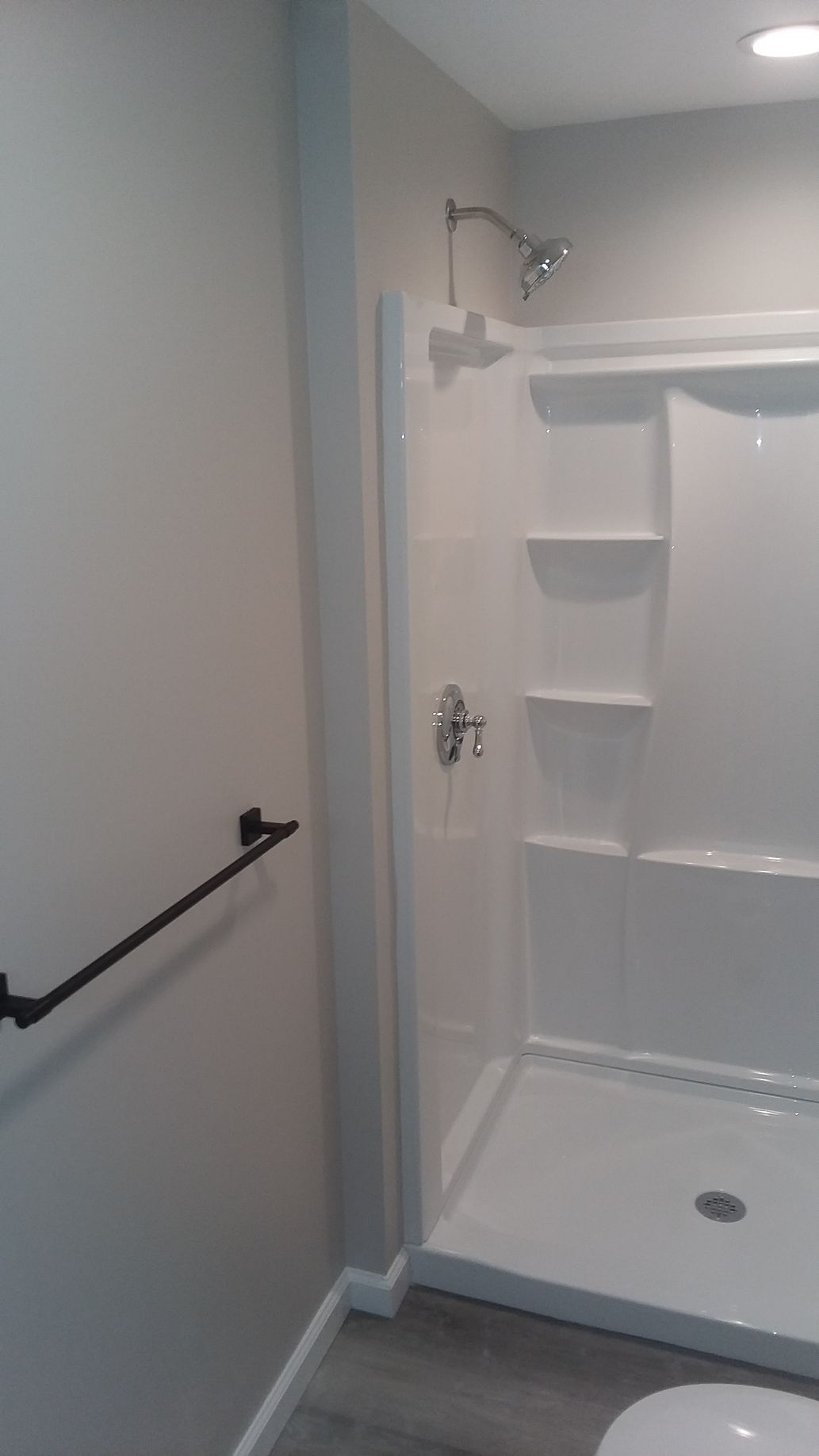 A white shower stall in a bathroom with a black towel rack on a gray wall.