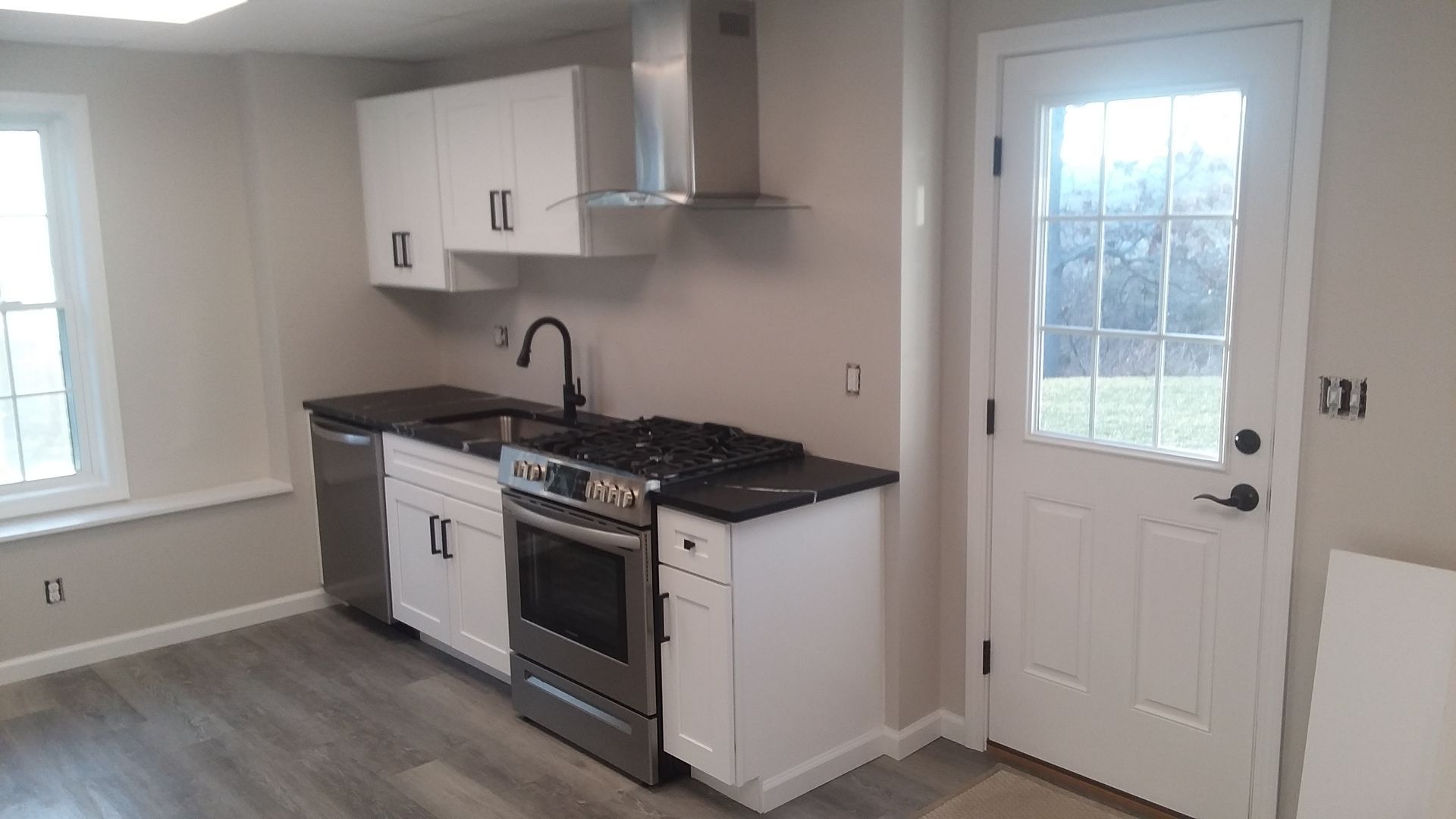 Small kitchen with white cabinets, stainless steel appliances, dark countertop, and a white door with a window.