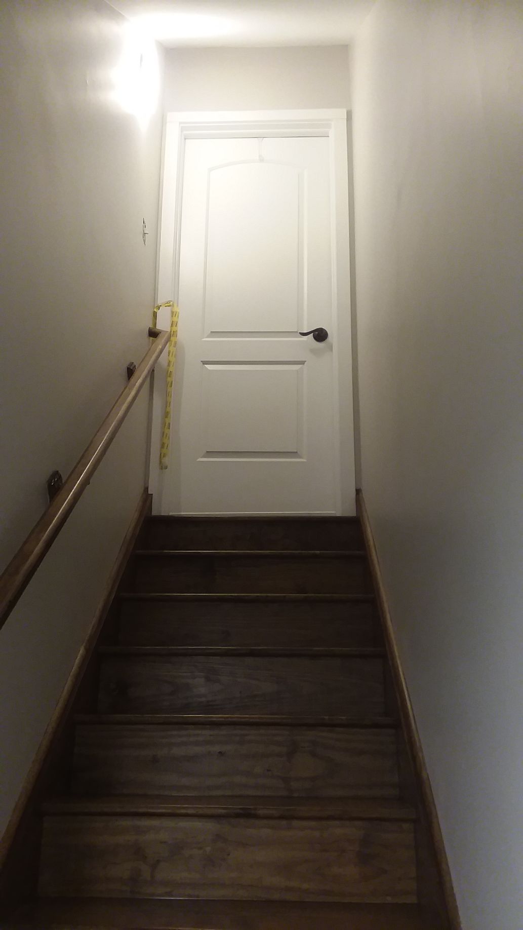 Staircase leading up to a closed white door. Wooden stairs and handrail. Dim lighting.