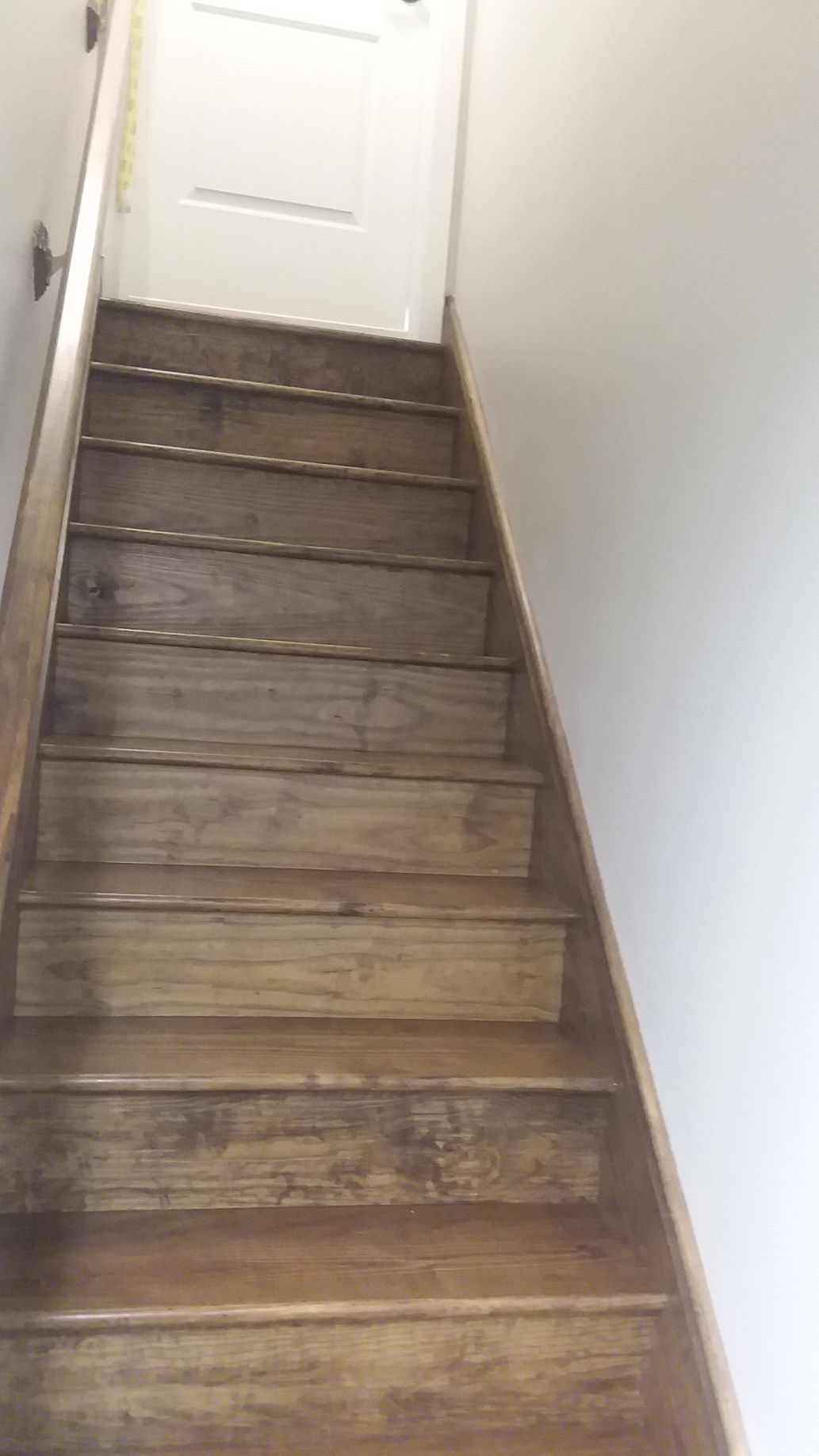 Wooden staircase leading upwards to a white door; brown wood steps, light walls.