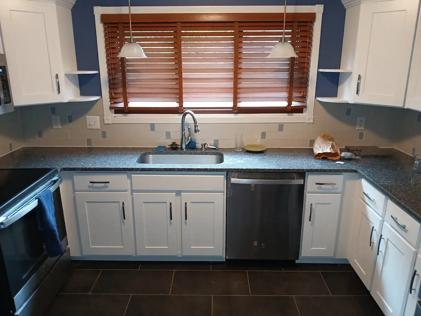 White kitchen cabinets with granite countertop, stainless steel sink and appliances, and wood blinds.
