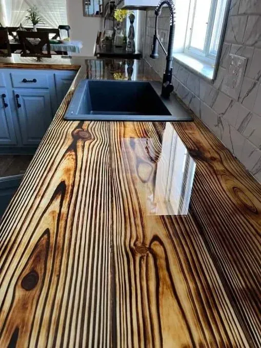 Close-up of a kitchen countertop made of wood planks with a glossy, epoxy-resin finish, and a black sink.