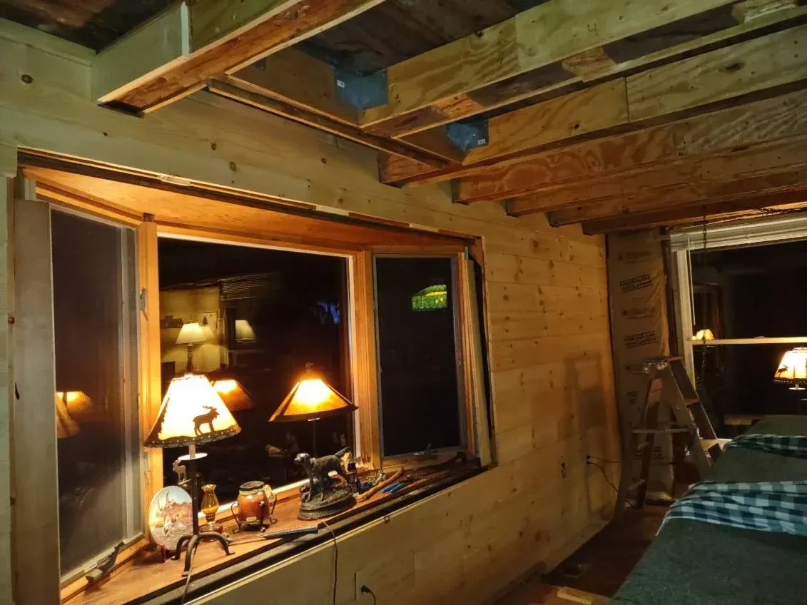 Interior view of a room with unfinished wood walls, window looking out onto a nighttime scene, and visible ceiling beams.