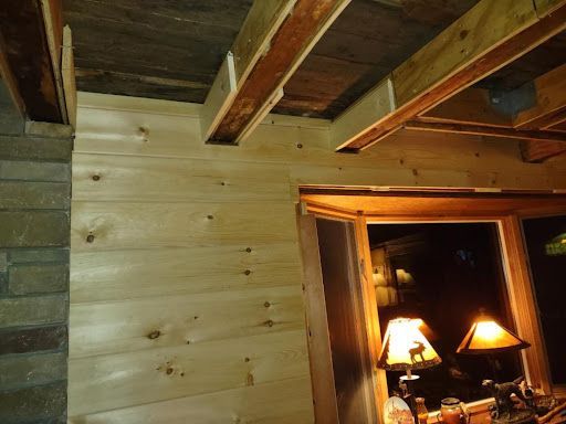 Wooden plank wall with window and warm lamp light. Part of a stone wall on the left.