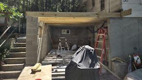 Construction of a wooden roof over a block-walled structure; a red ladder leans against the wall.