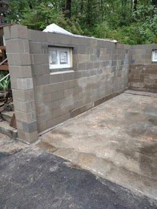 Cinder block wall with small window, on a concrete slab in an outdoor setting.