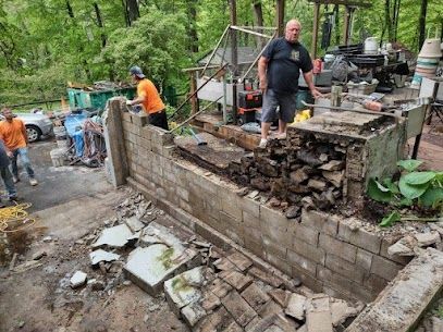 Men demolishing a brick structure outdoors. Debris and tools are visible. Overcast day.