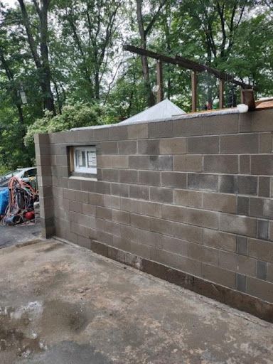Gray cinder block wall with a small window, built on a concrete foundation.