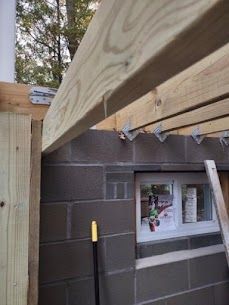 Wooden beams supported by metal brackets on a cinder block structure. A small window is visible.