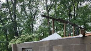 A partially visible, concrete-block building with a wooden frame and trees in the background.