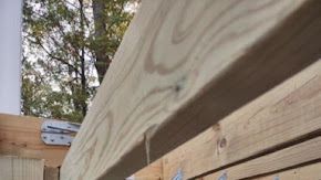 Close-up view of wooden beams, showing wood grain, with trees and sky in the background.