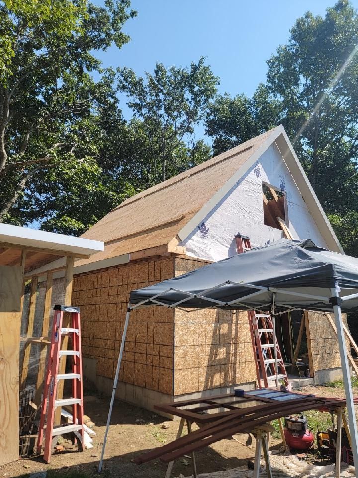 Construction of a building with a brown roof and unfinished walls. A person is working on the roof.