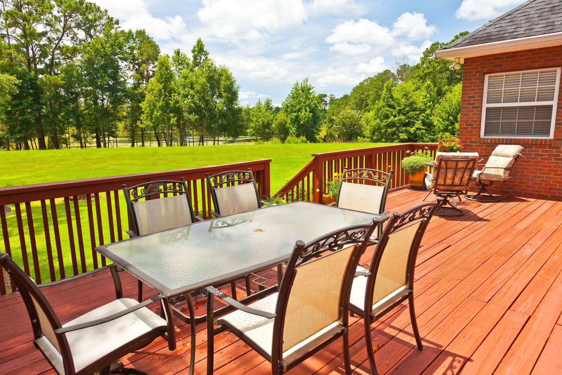 Wooden deck with outdoor dining table and chairs overlooking a green field, under a sunny sky.