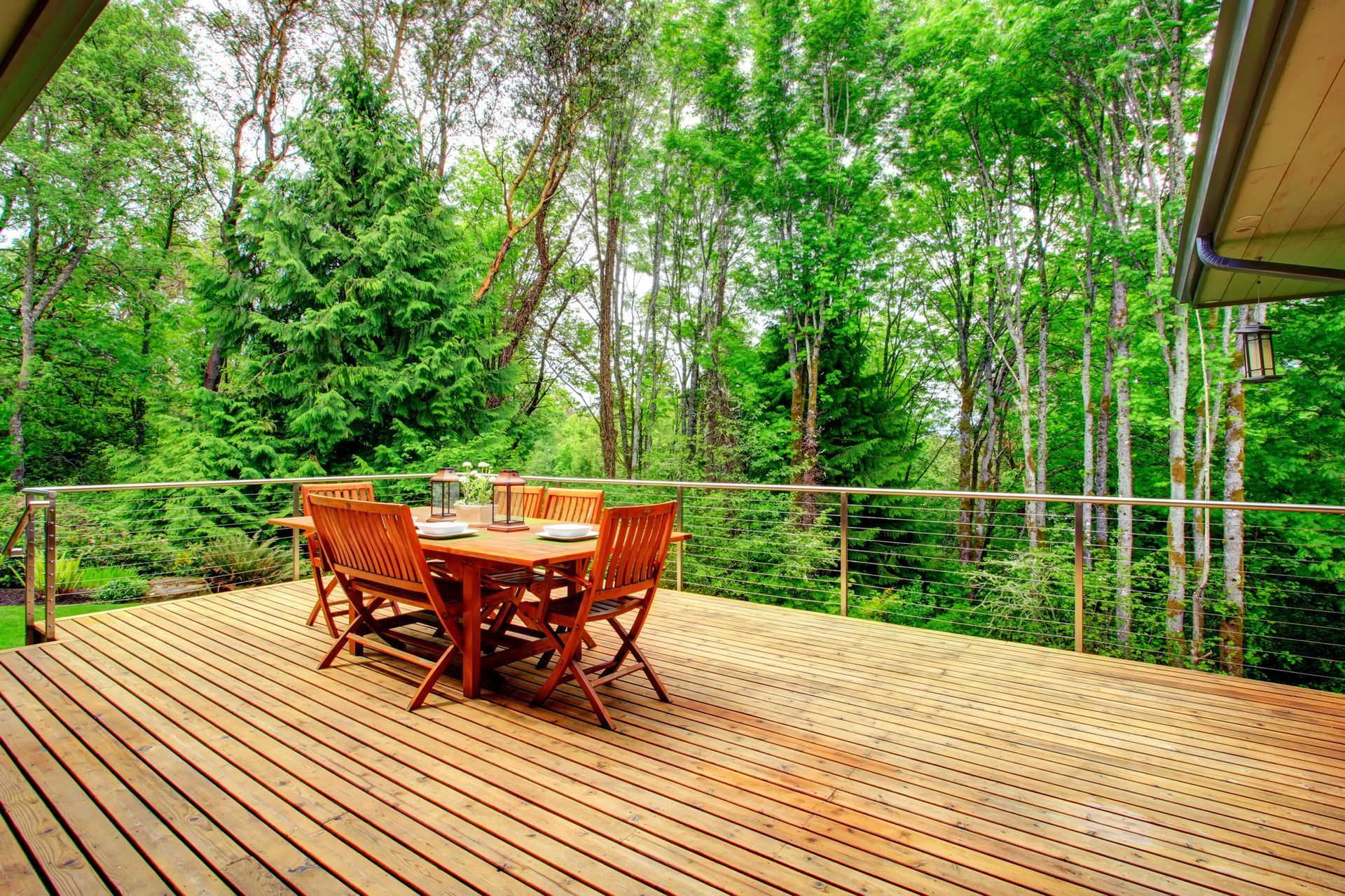 Wooden deck with table and chairs, surrounded by lush green trees.