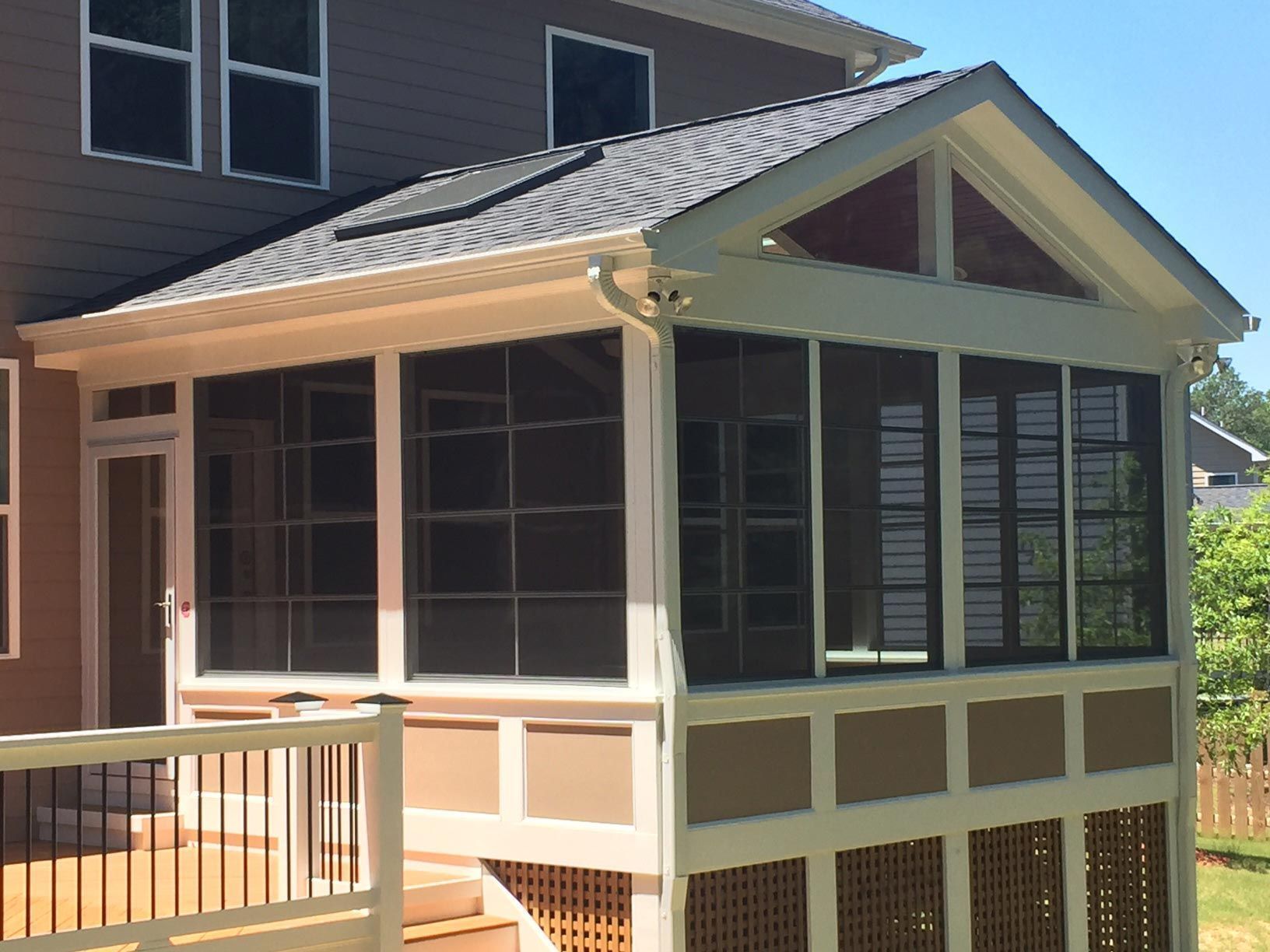 Screened-in porch addition with tan and brown siding, attached to a house with a deck.