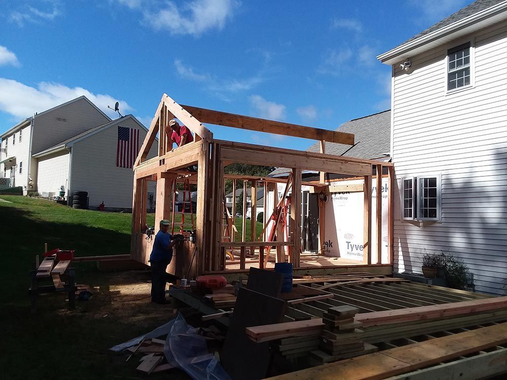 Construction of a wood-framed structure in a backyard, with workers installing the roof.