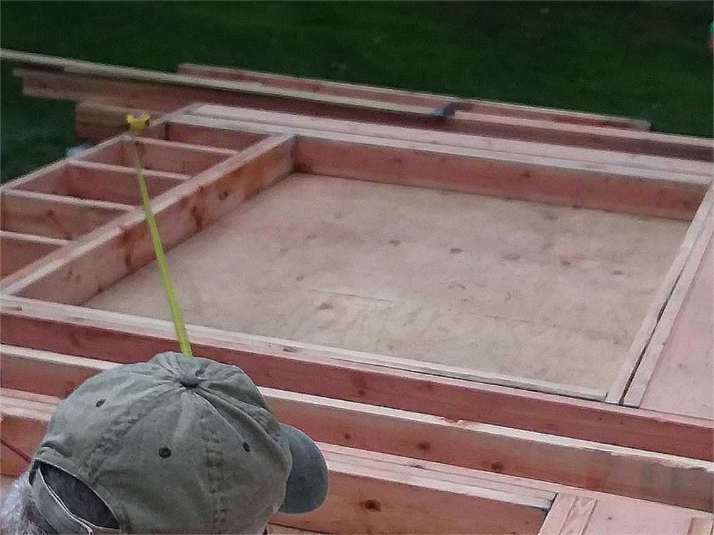 Person measuring a wooden frame for construction with a yellow tape measure, outdoors.