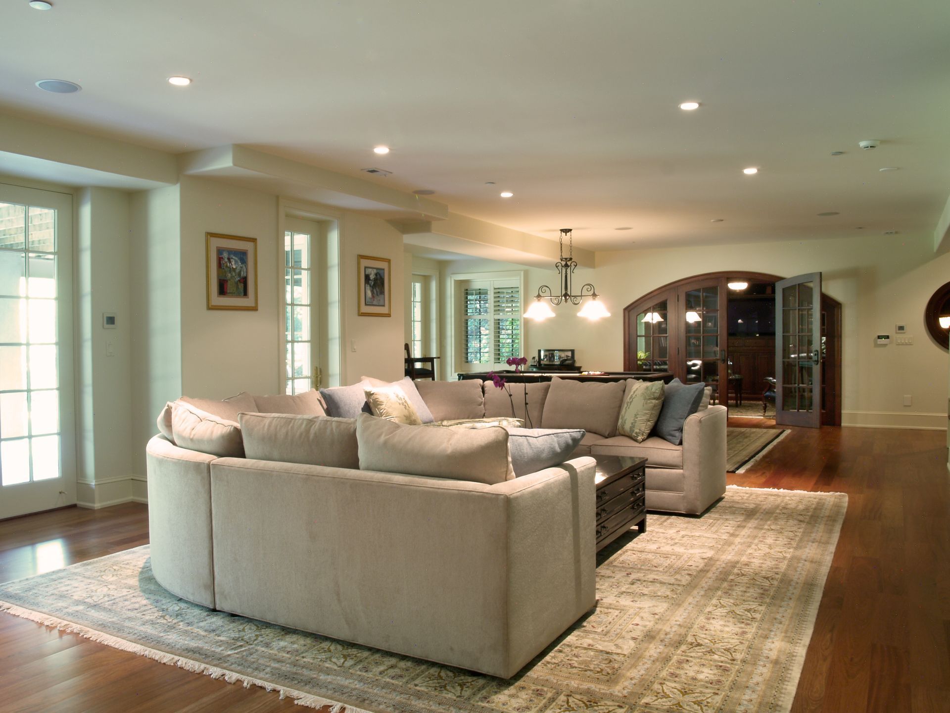 Spacious living room with beige sofa, patterned rug, hardwood floor, French doors, and recessed lighting.