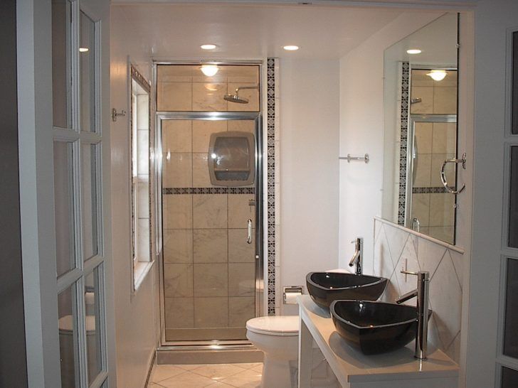 Small bathroom with shower, toilet, and dual sinks. Light walls, beige tile, black sinks.