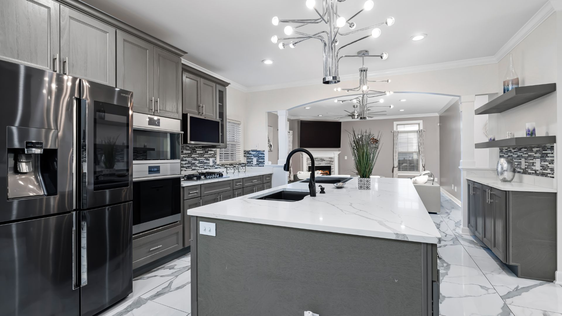 Modern gray kitchen with stainless steel appliances, large island, and marble countertops.