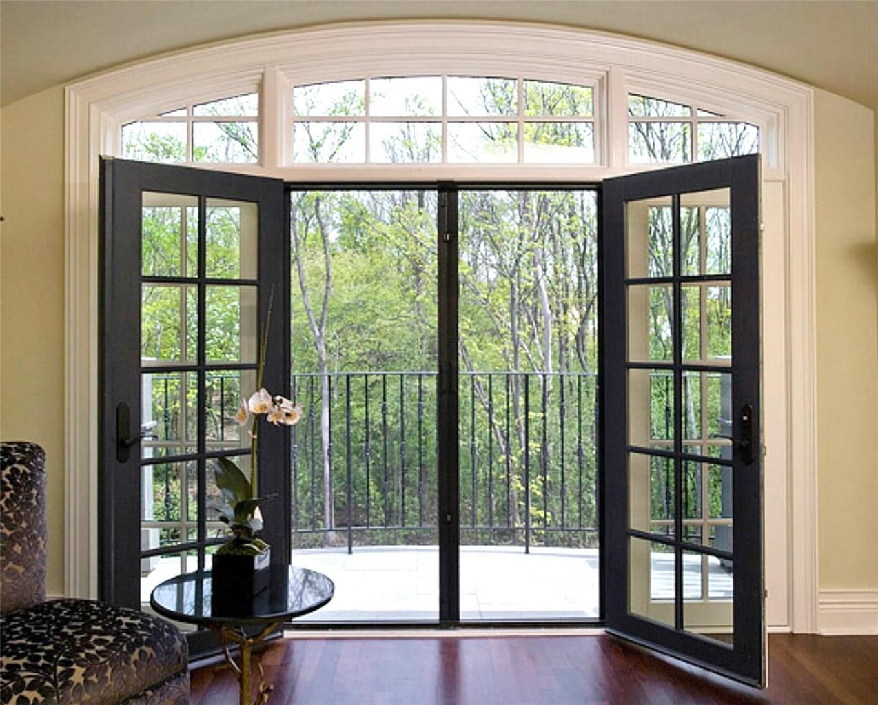 Black French doors open to a balcony with trees. A table and chair are visible inside.