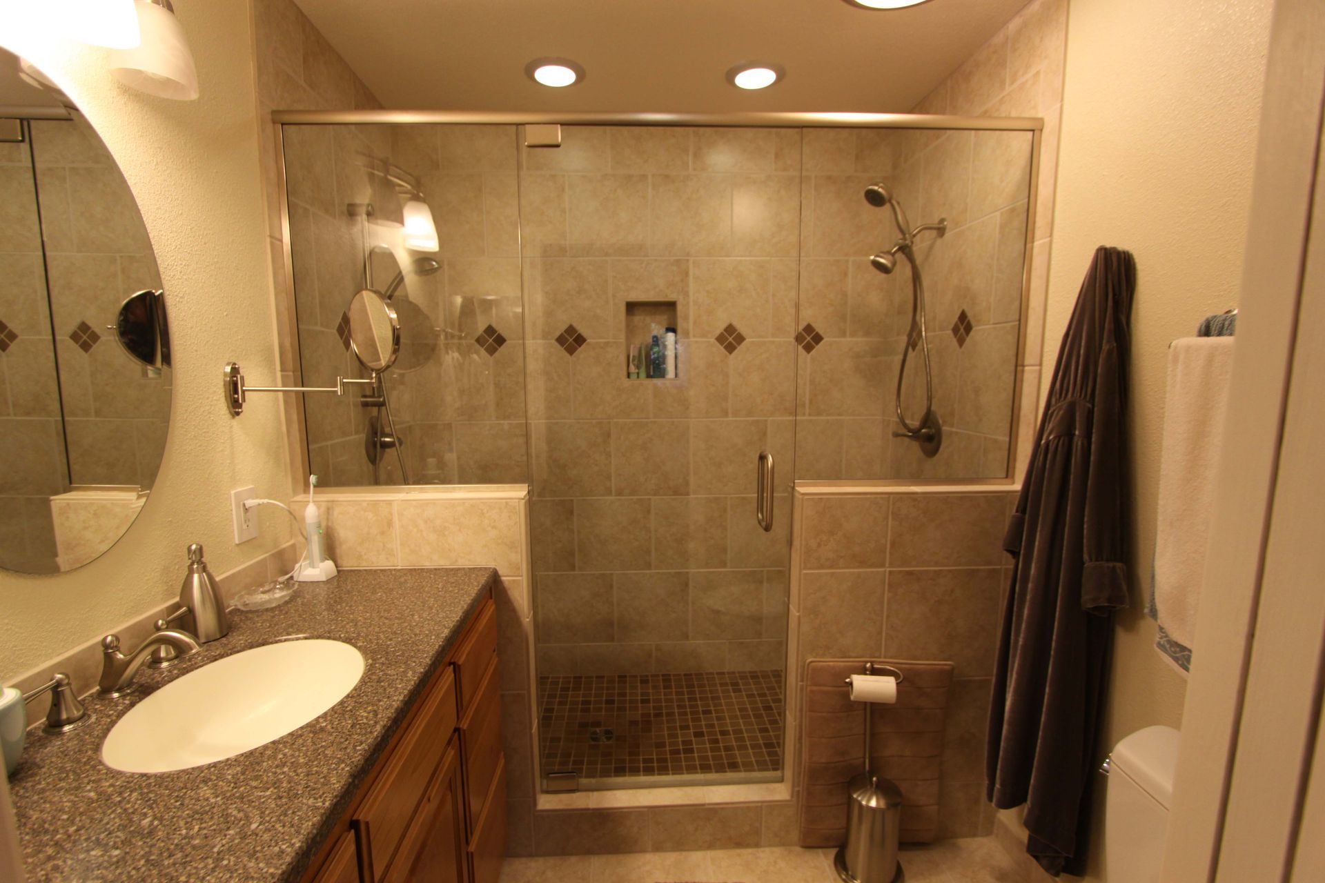 Bathroom with beige tiled shower, vanity, and brown wooden cabinet. Glass shower door, oval mirror.