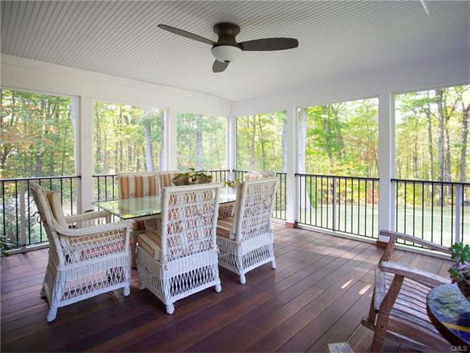 Screened porch with dining table and chairs overlooking a wooded area.