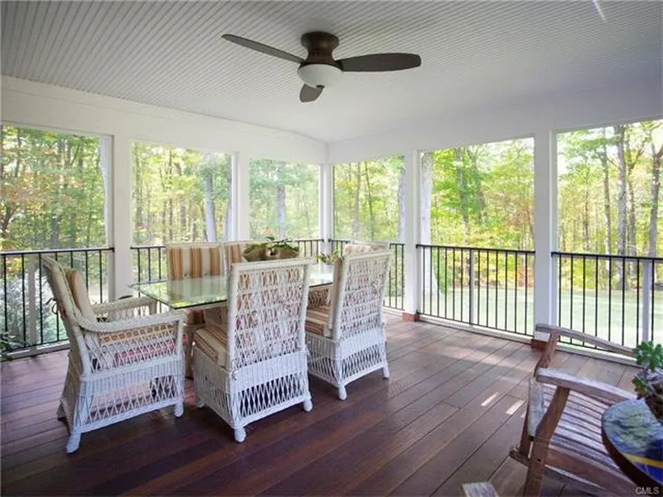 Screened-in porch with wicker furniture and a ceiling fan, overlooking a wooded area.