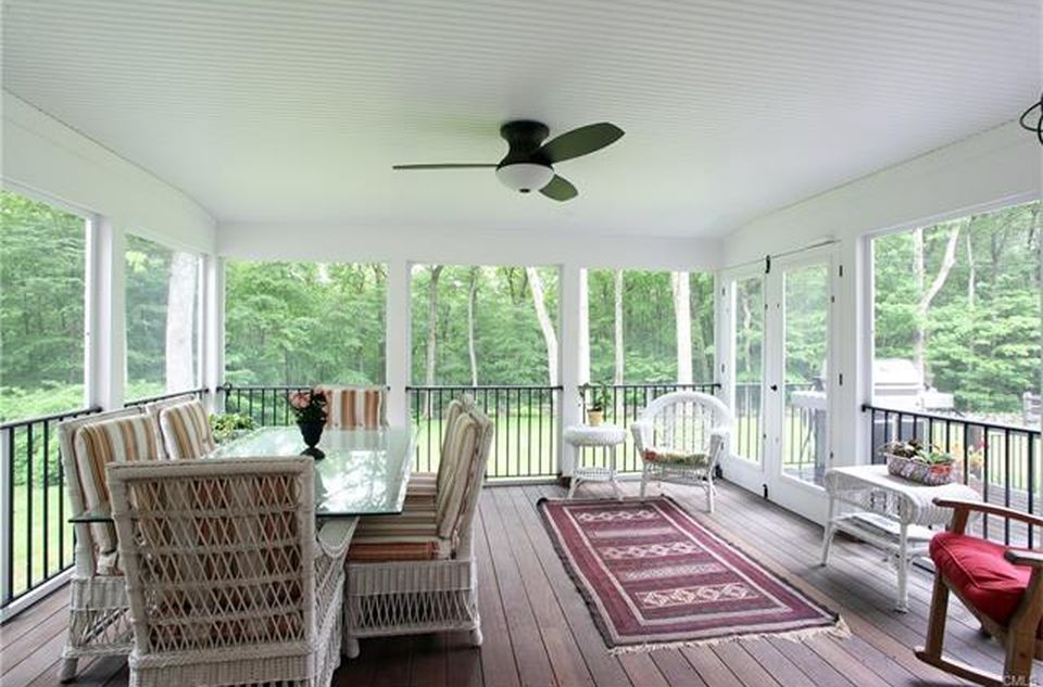 Screened-in porch with dining table and seating, overlooking a wooded area.