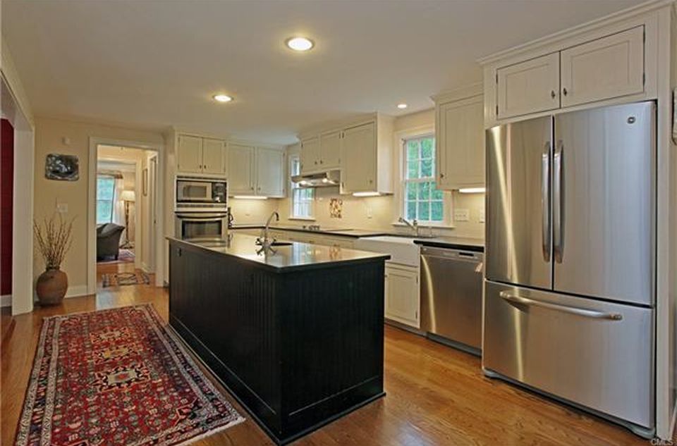 Kitchen with black island, stainless steel appliances, white cabinets, and wooden floors.