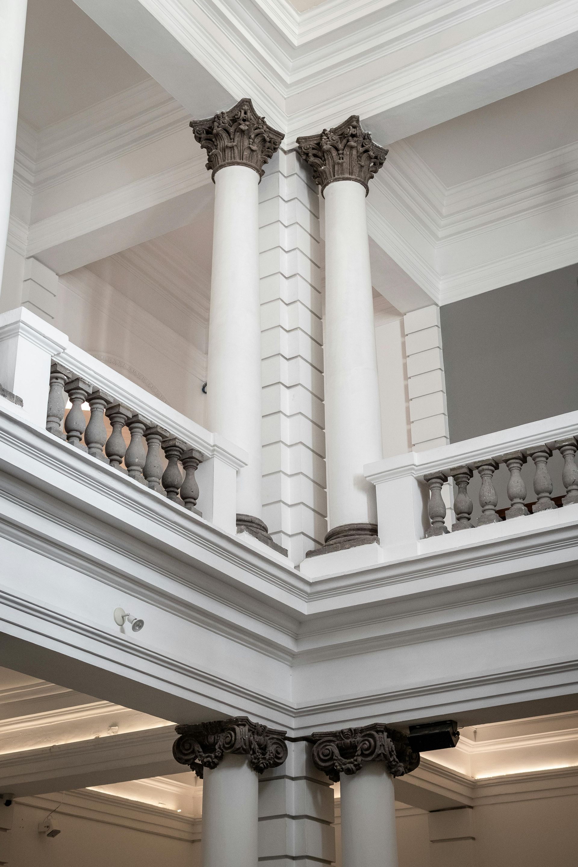 Interior view of a building with white pillars, ornate balustrades, and detailed moldings.