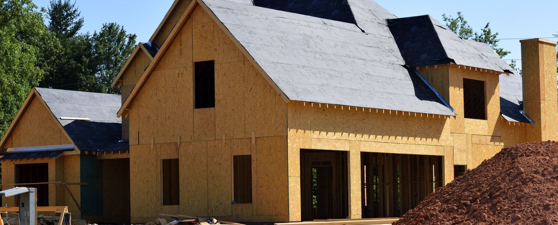 House under construction with exposed wooden framing and dark roofing.