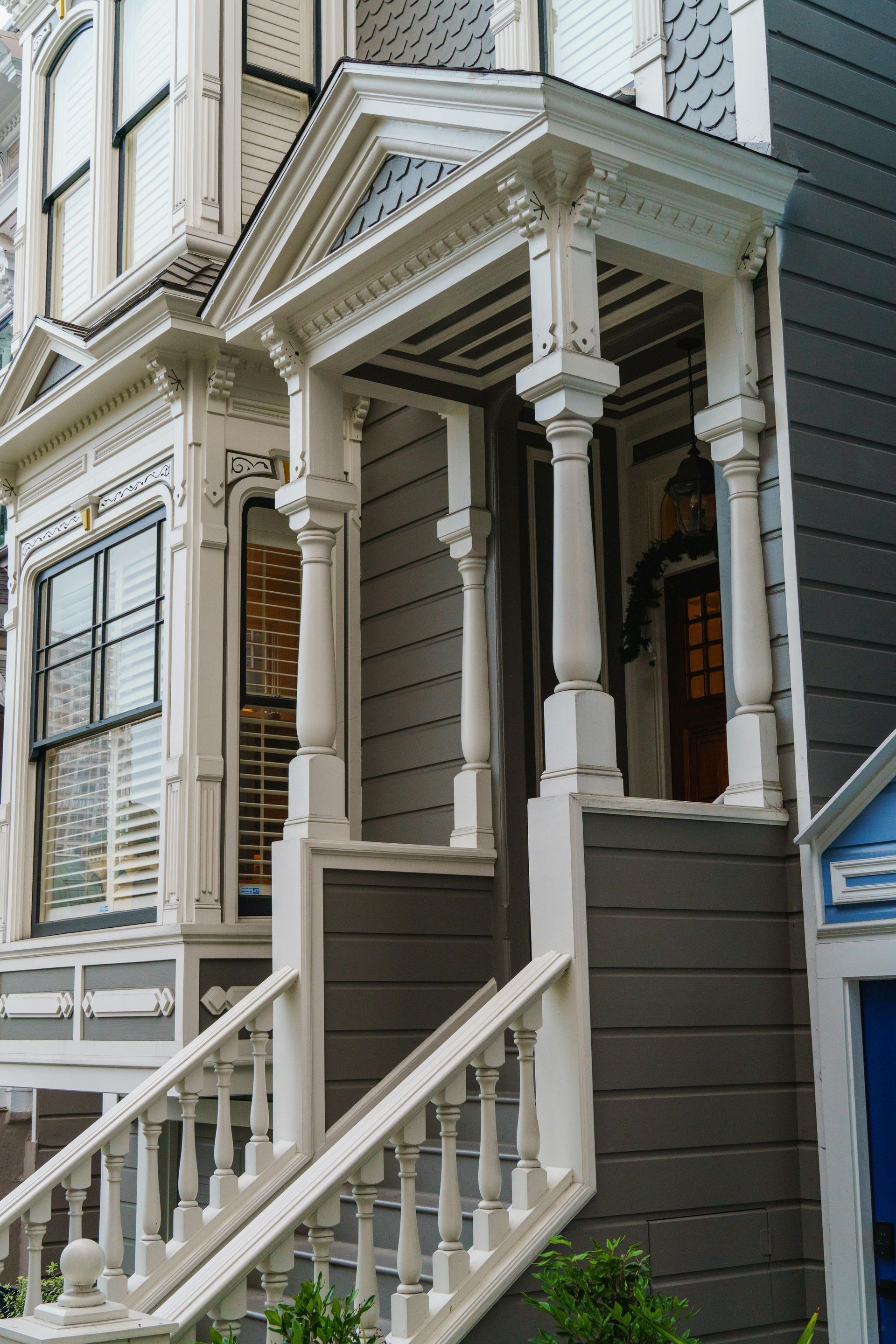 Victorian house exterior with ornate white trim, gray siding, and porch with stairs.