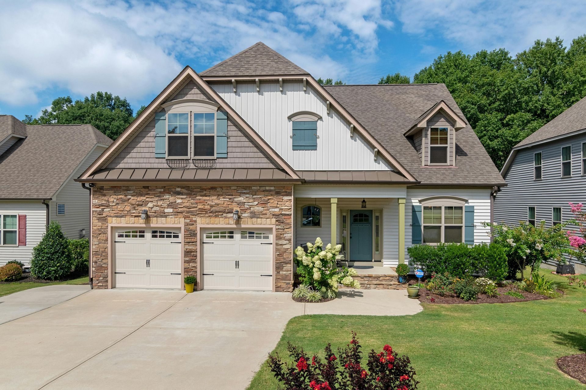 A beige and stone house with a two-car garage, blue shutters, and a well-kept lawn.
