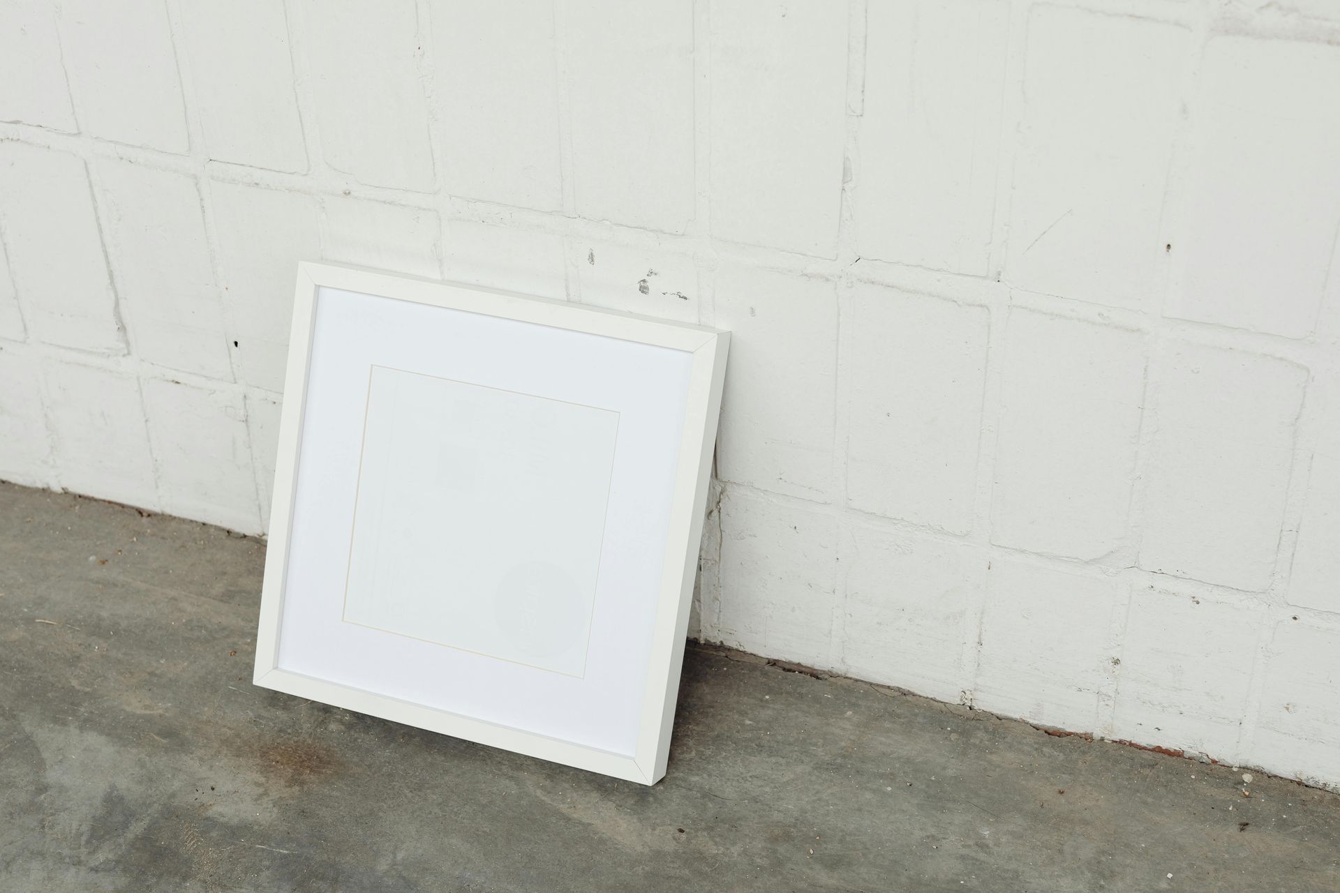 White rectangular frame leaning against a white brick wall on a concrete surface.