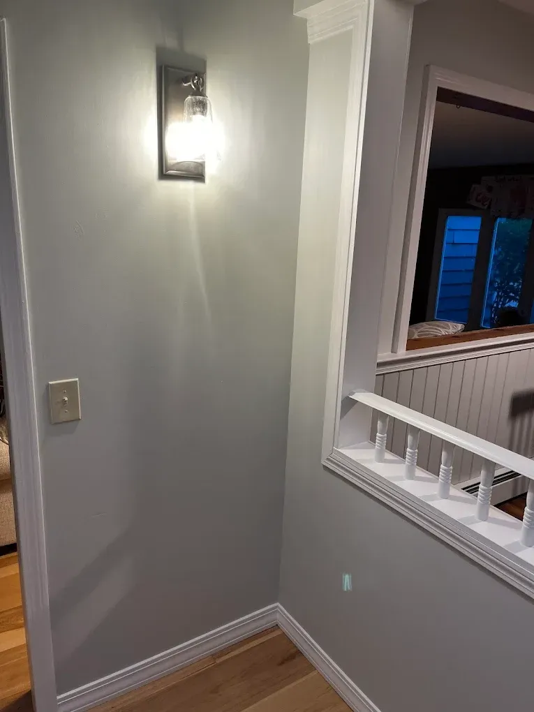 A gray wall with a sconce and light switch. White trim surrounds the corner and railing.