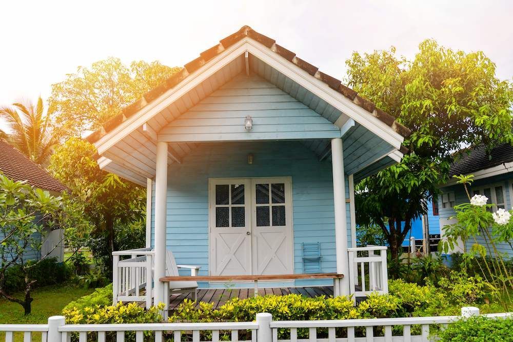 A Small Blue House With a White Fence in Front of It — Shane Rice Builder & Renovation Specialist In Southside, QLD