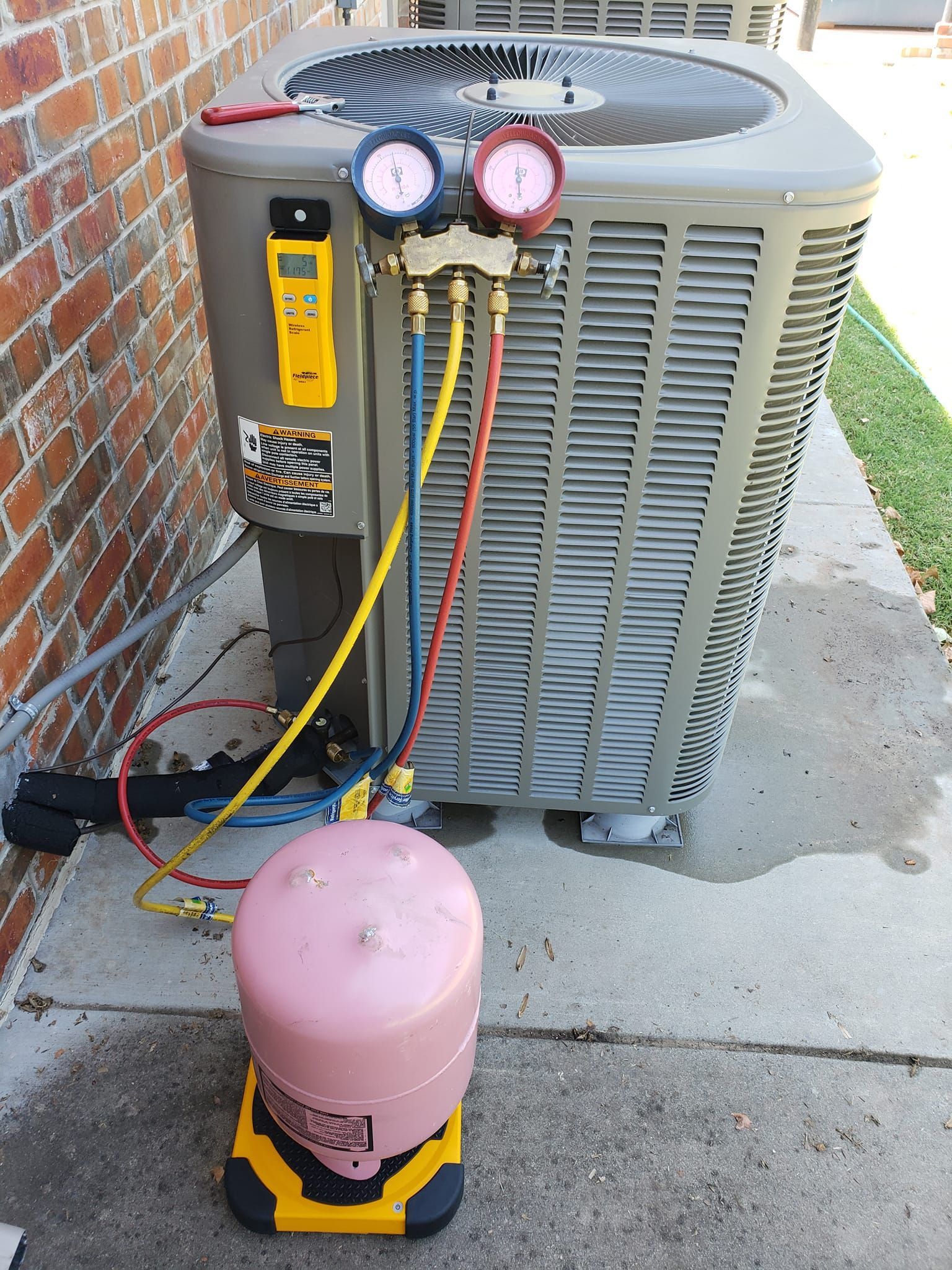 An air conditioner is being installed on a sidewalk next to a brick wall.