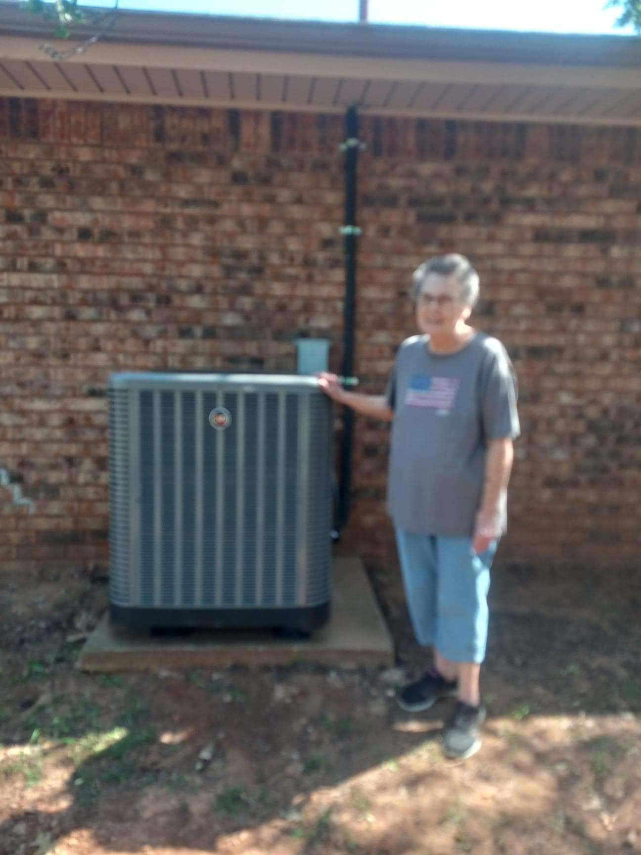 A woman is standing next to an air conditioner in front of a brick building.