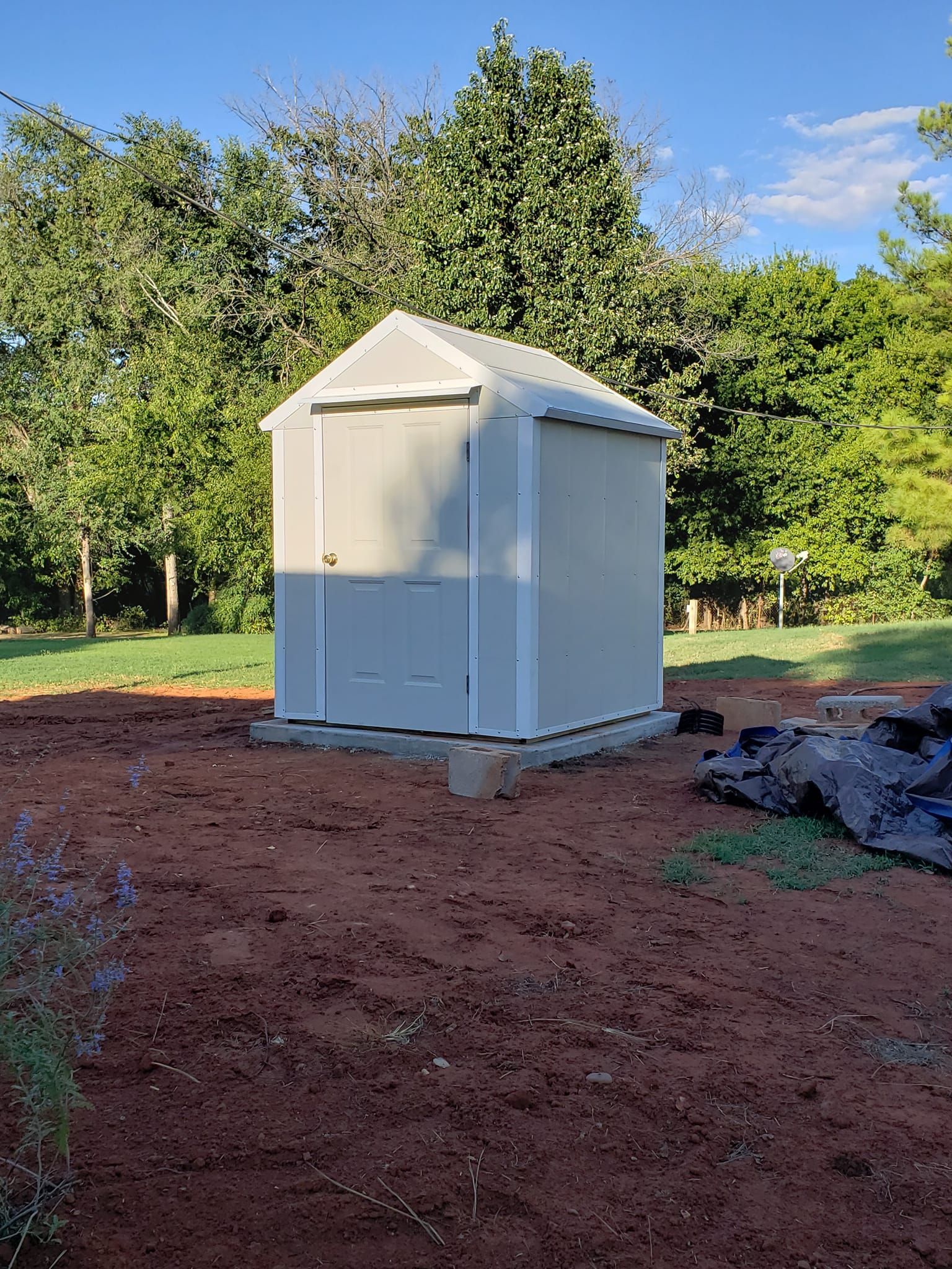A small white shed is sitting in the middle of a dirt field.