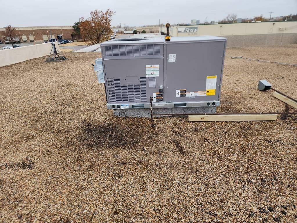 An air conditioner is sitting on top of a gravel covered roof.