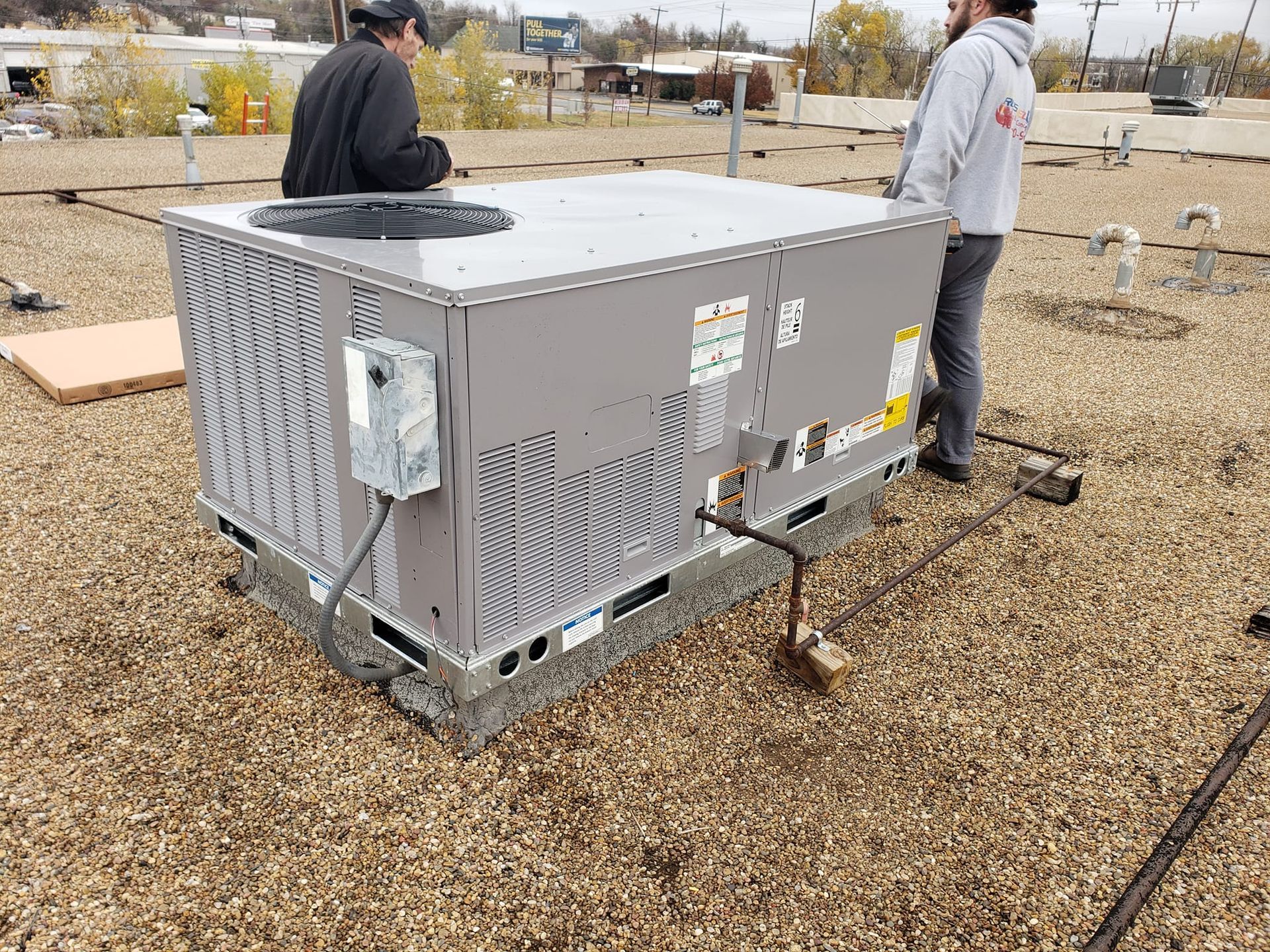 Two men are standing next to a large box on top of a gravel roof.